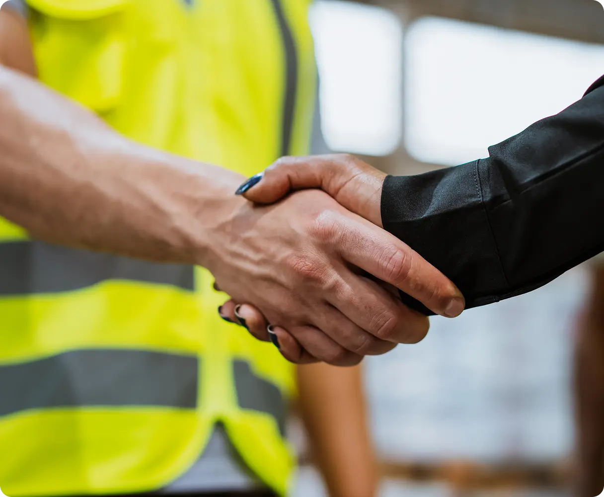 Handshake between a worker in a safety vest and a person in formal attire.