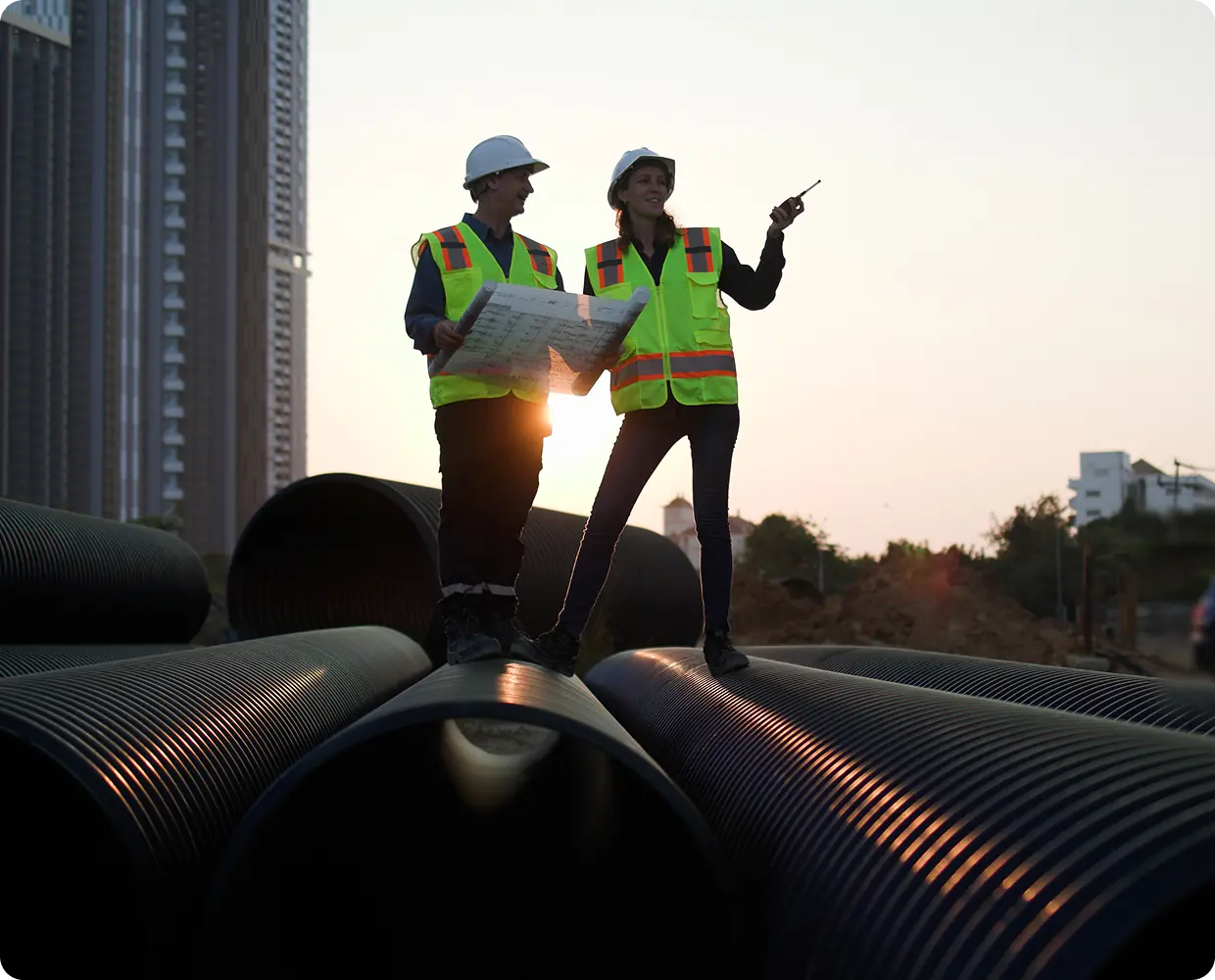 Engineers inspecting large pipelines at a construction site during sunset.