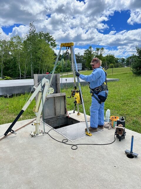 A man operating a tripod-mounted drilling rig outdoors.