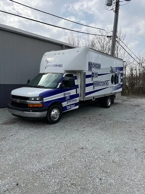 A moving truck parked on a gravel area outside a building.
